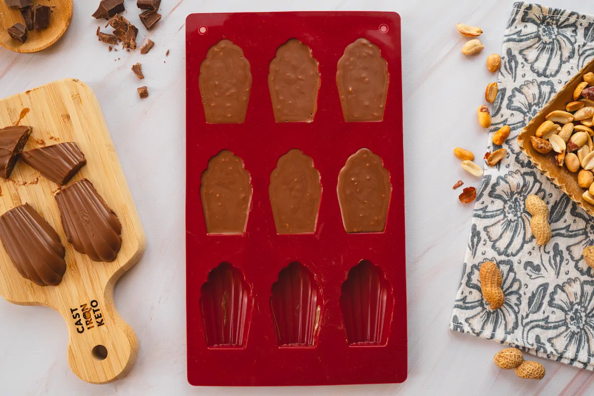 Homemade keto chocolate fudges are showcased on a wooden board, with a few taken out from a silicone mold, which is now partially empty.
