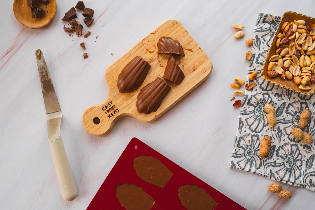 Keto chocolate fudges are displayed on a wooden board, where some are cut alongside a cake spatula.