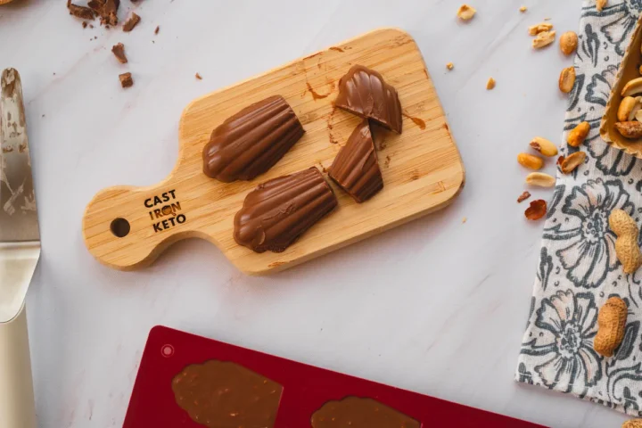 Homemade keto chocolate fudges are displayed on a wooden board, where some are cut.