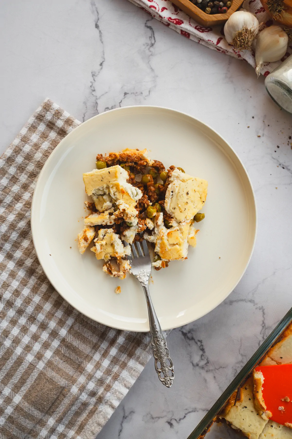 Keto cottage pie on a white plate, with the top layer moved to reveal the ground beef and mushroom mixture.
