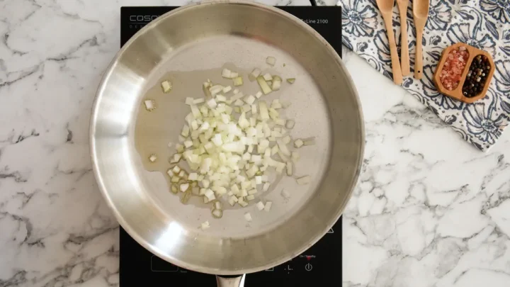 Sautéing diced onion in a stainless steel pan with olive oil.