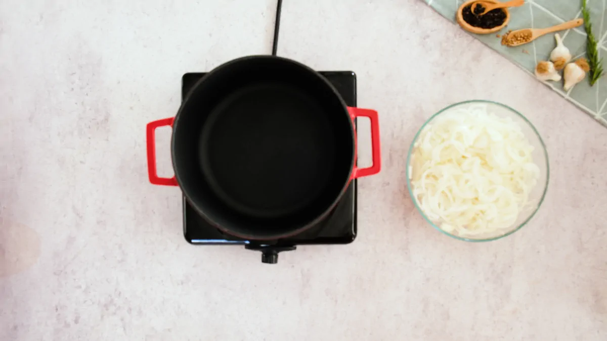 An empty pot getting heated on an induction stovetop alongside a big bowl of sliced onions.