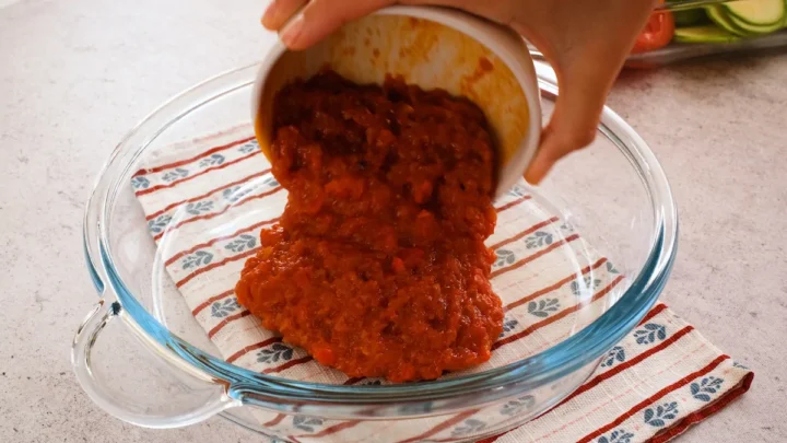 Transferring the prepared tomato sauce from a bowl to the baking dish.
