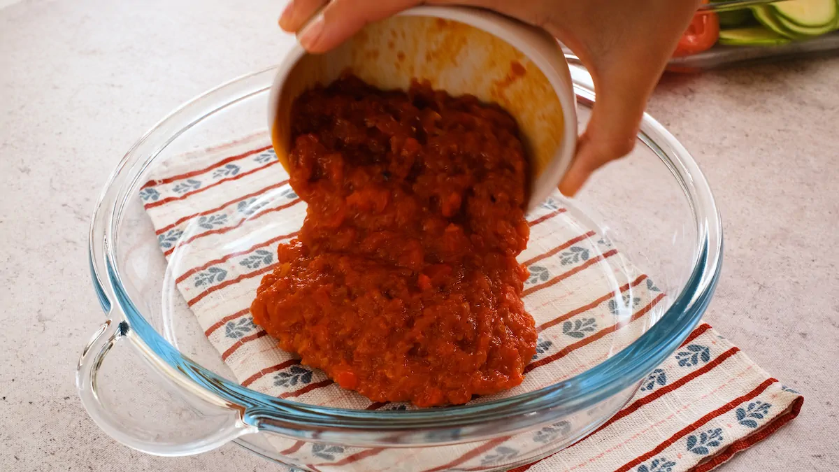 Transferring the prepared tomato sauce from a bowl to the baking dish.