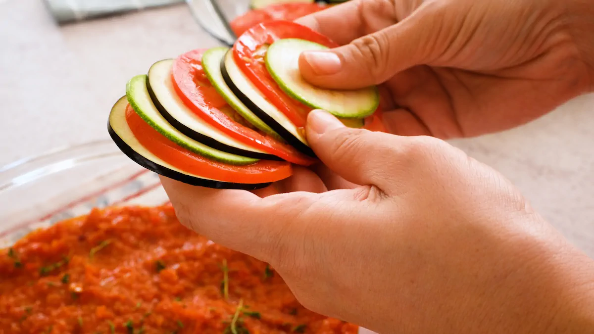 Arranging sliced egg plant, tomato and zucchini alternating and overlapping onto the sauce in a baking dish.