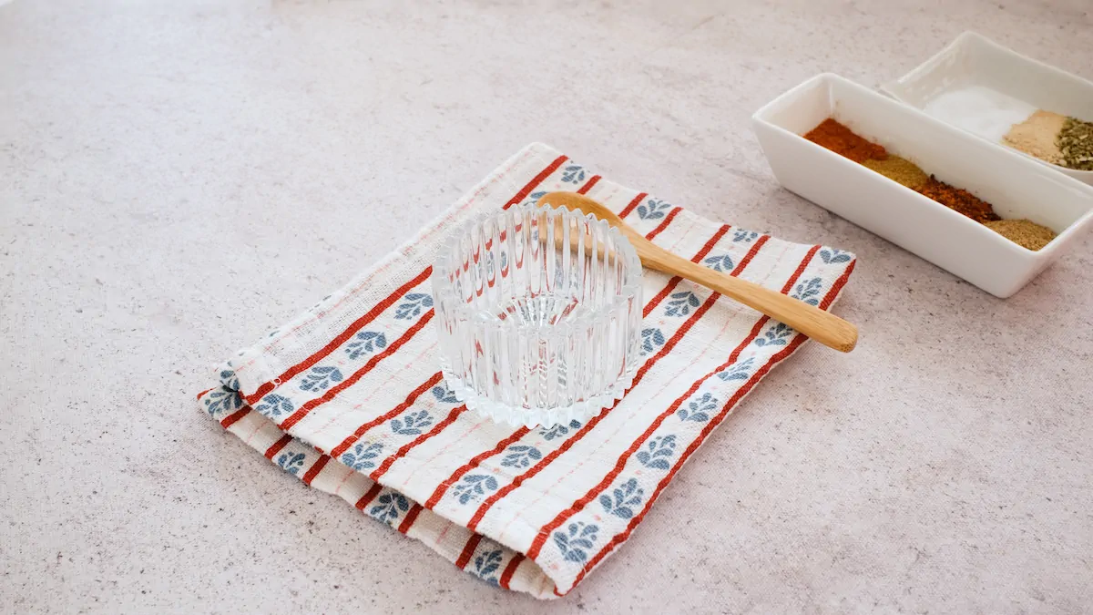 A small empty bowl and a spoon alongside the required amount of spices for the Tex-Mex seasoning.