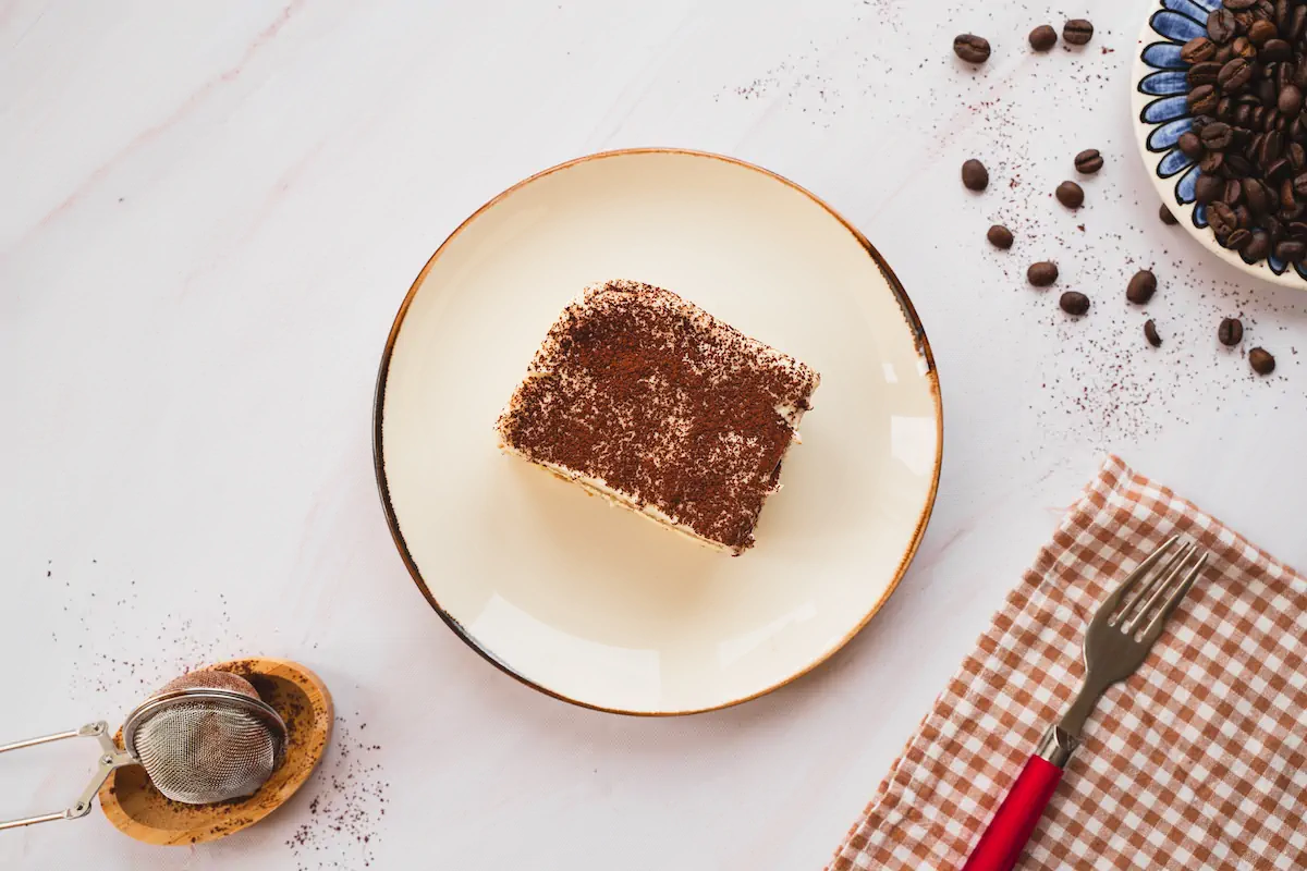 Keto tiramisu, dusted with cocoa powder, is presented on a plate alongside a fork.