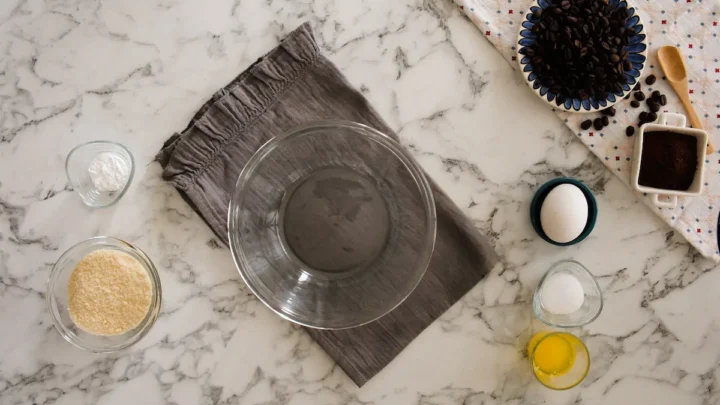 An empty mixing bowl alongside almond flour, sweetener, baking powder, pinch of salt, butter, egg, and vanilla.