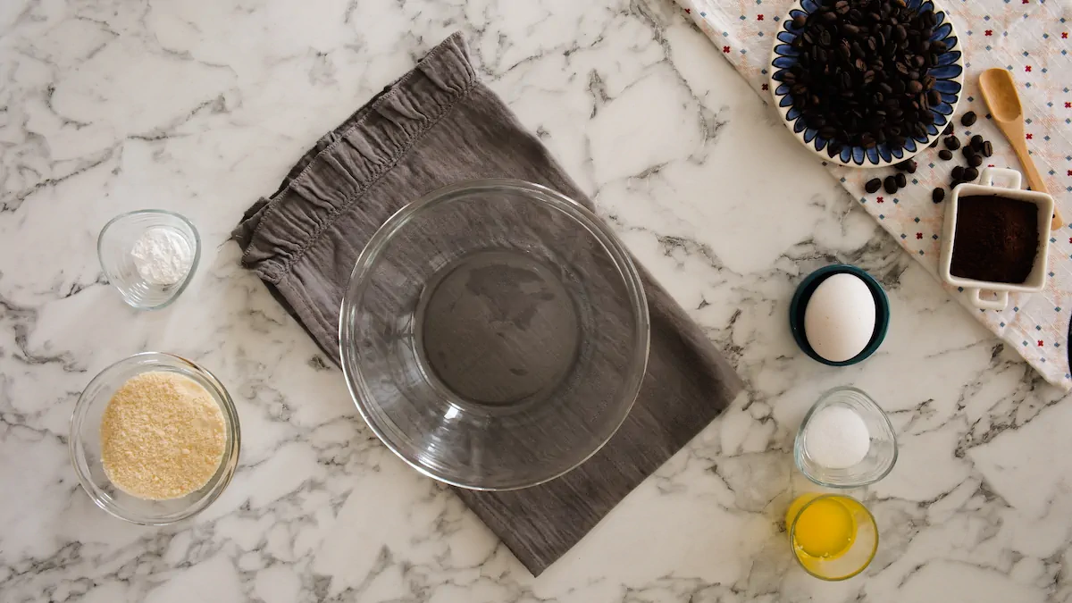 An empty mixing bowl alongside almond flour, sweetener, baking powder, pinch of salt, butter, egg, and vanilla.