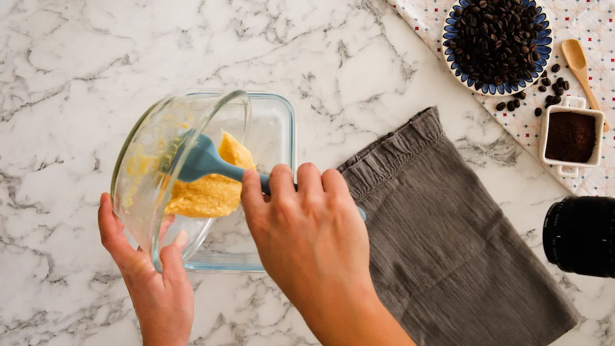 Pouring the cake batter into a greased microwave-safe glass dish with a silicone spatula.