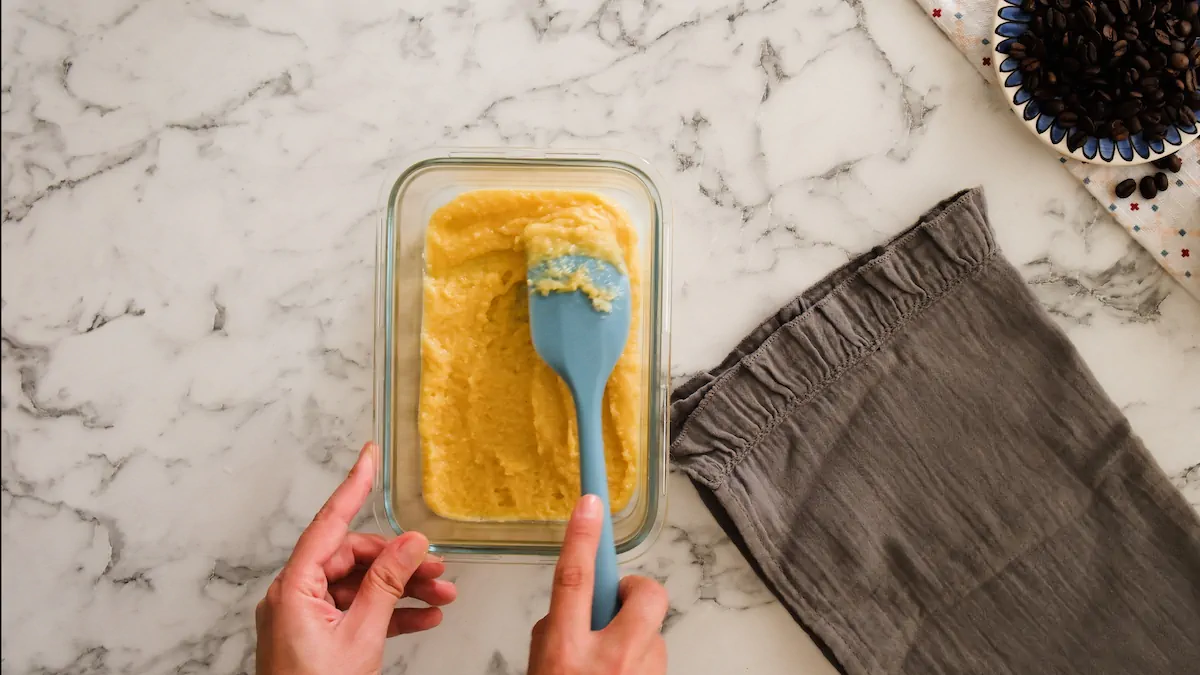 Leveling the cake batter with a silicone spatula in a greased glass bowl.