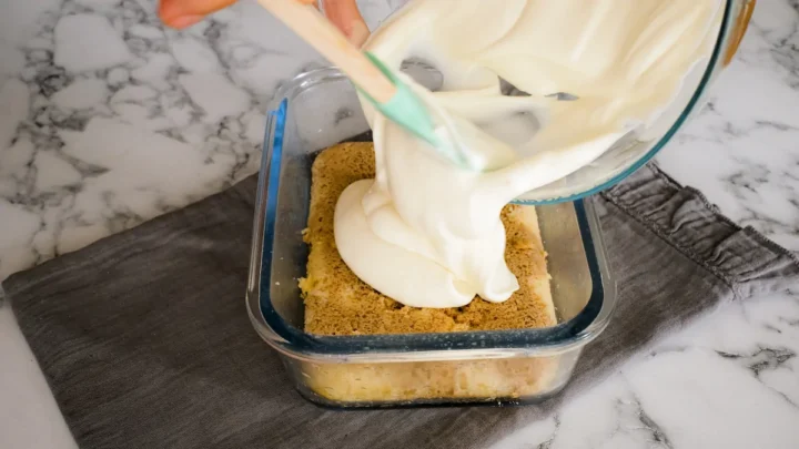 Pouring the mascarpone cream mixture onto the bottom layer of tiramisu.