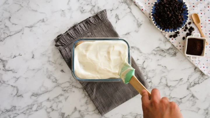 Spreading the mascarpone cream mixture onto the top layer of tiramisu with a spatula.