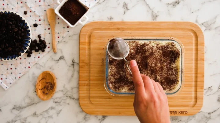 Dusting the keto tiramisu with cocoa powder.