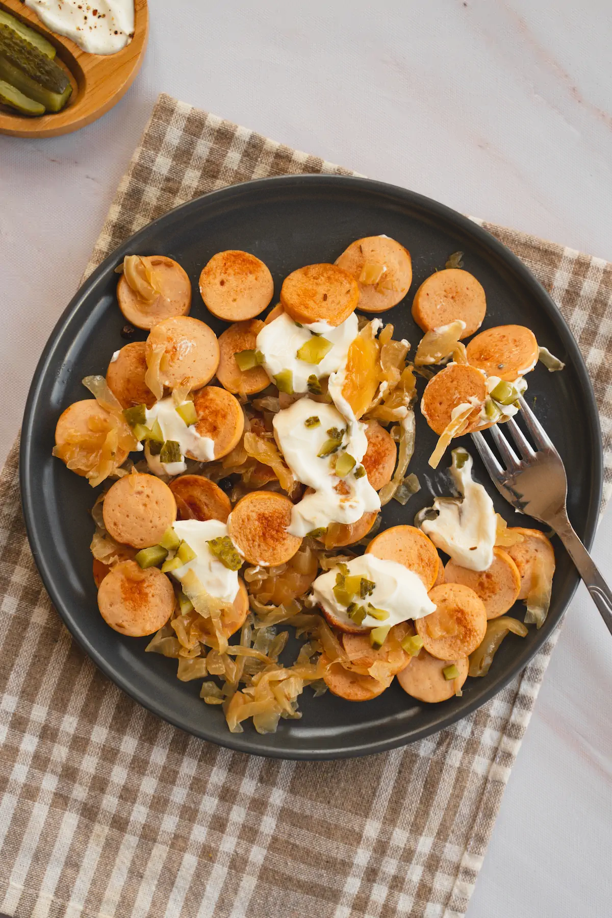 Keto sauerkraut and sausage presented on a plate topped with pickles and cream.