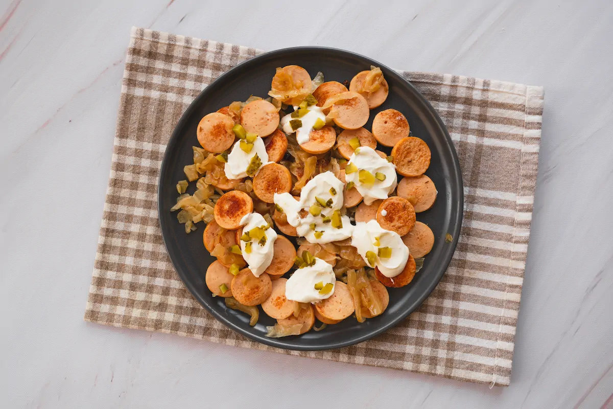 Homemade sausage and sauerkraut served on a plate topped with pickles and sour cream.