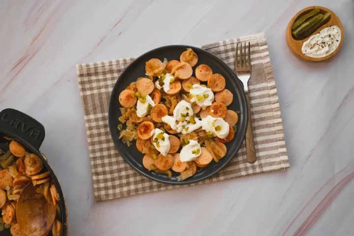 Low-carb sausage and sauerkraut served on a plate topped with pickles and sour cream.