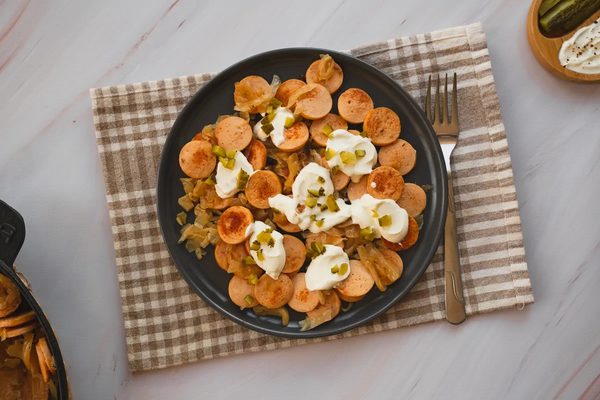 Sausage and sauerkraut presented on a plate topped with pickles and sour cream.