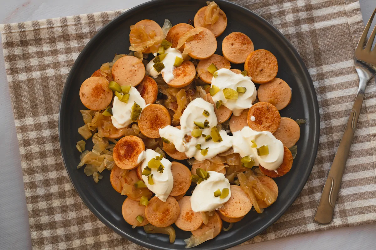 Sausage and sauerkraut on a plate topped with pickles and sour cream.