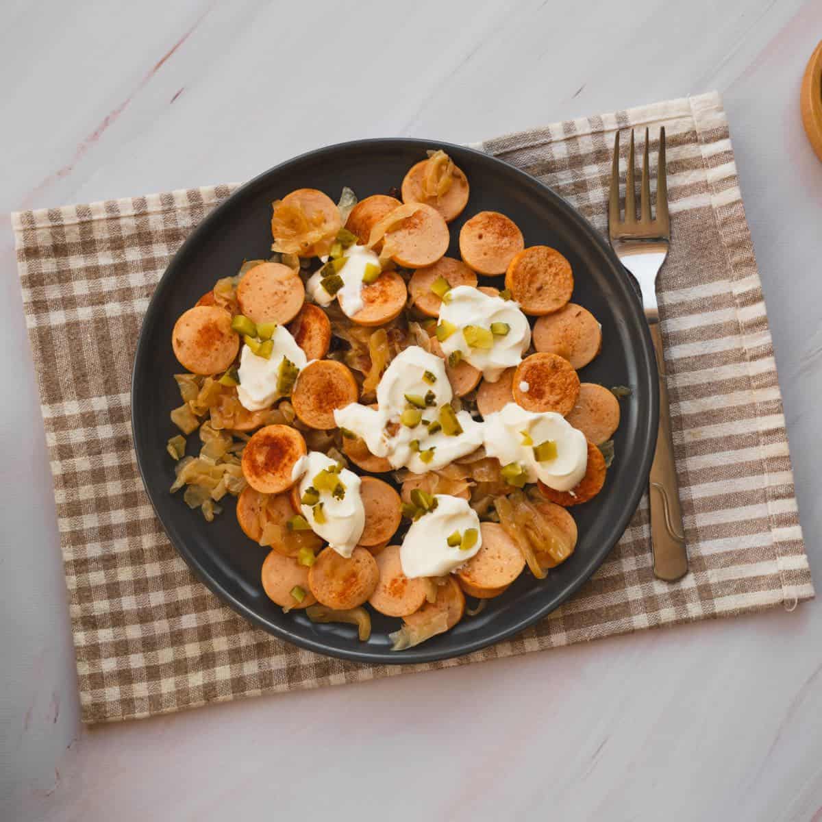 Sausage and sauerkraut served on a plate topped with pickles and a dollop of sour cream.