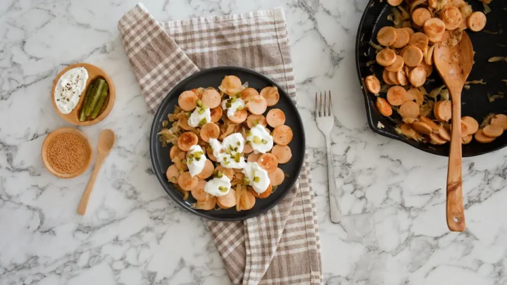 Serving sausage and sauerkraut on a plate garnished with sour cream and pickles.