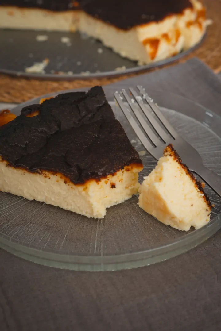 A piece of burnt Basque cheesecake, plated, cut with a fork, revealing its texture.