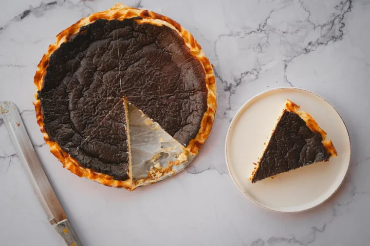 A slice of burnt Basque cheesecake served on a plate, cut from the whole cake.