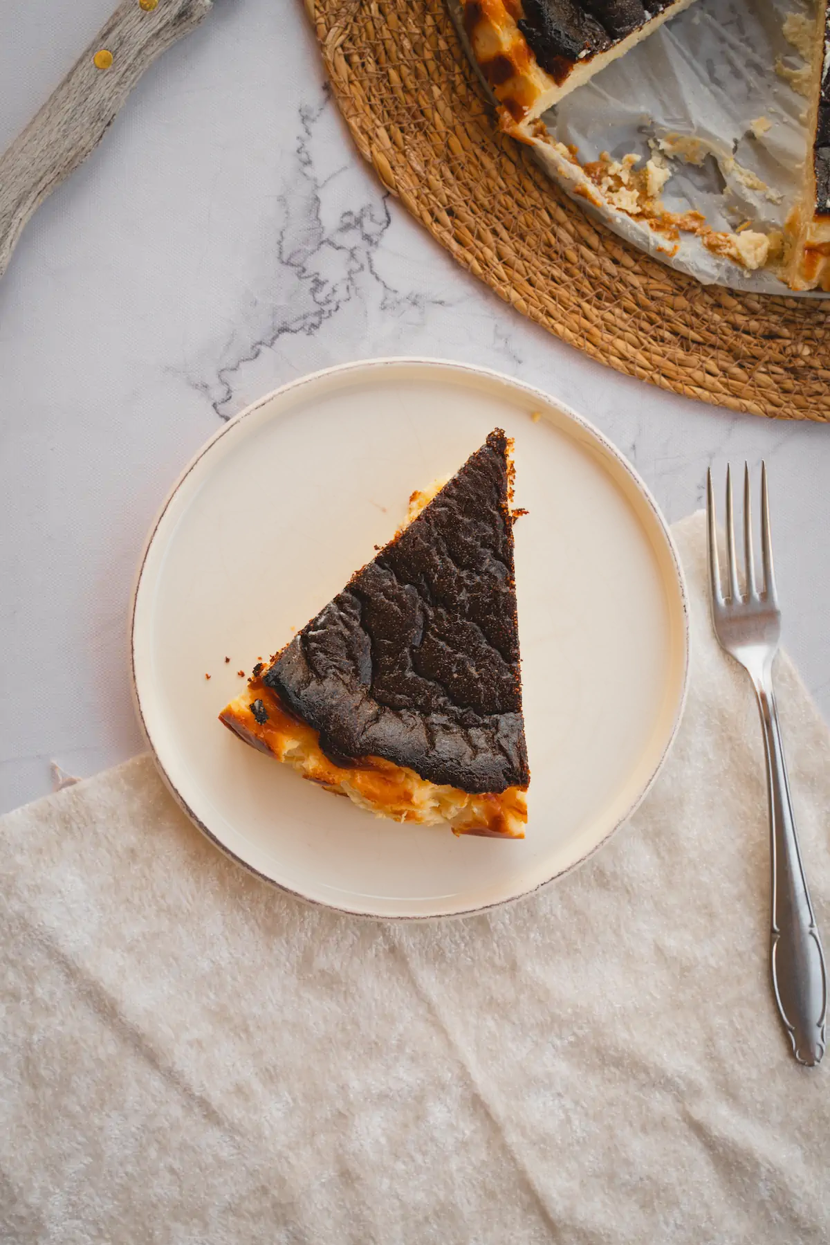 A slice of burnt Basque cheesecake presented on a white plate with a fork.