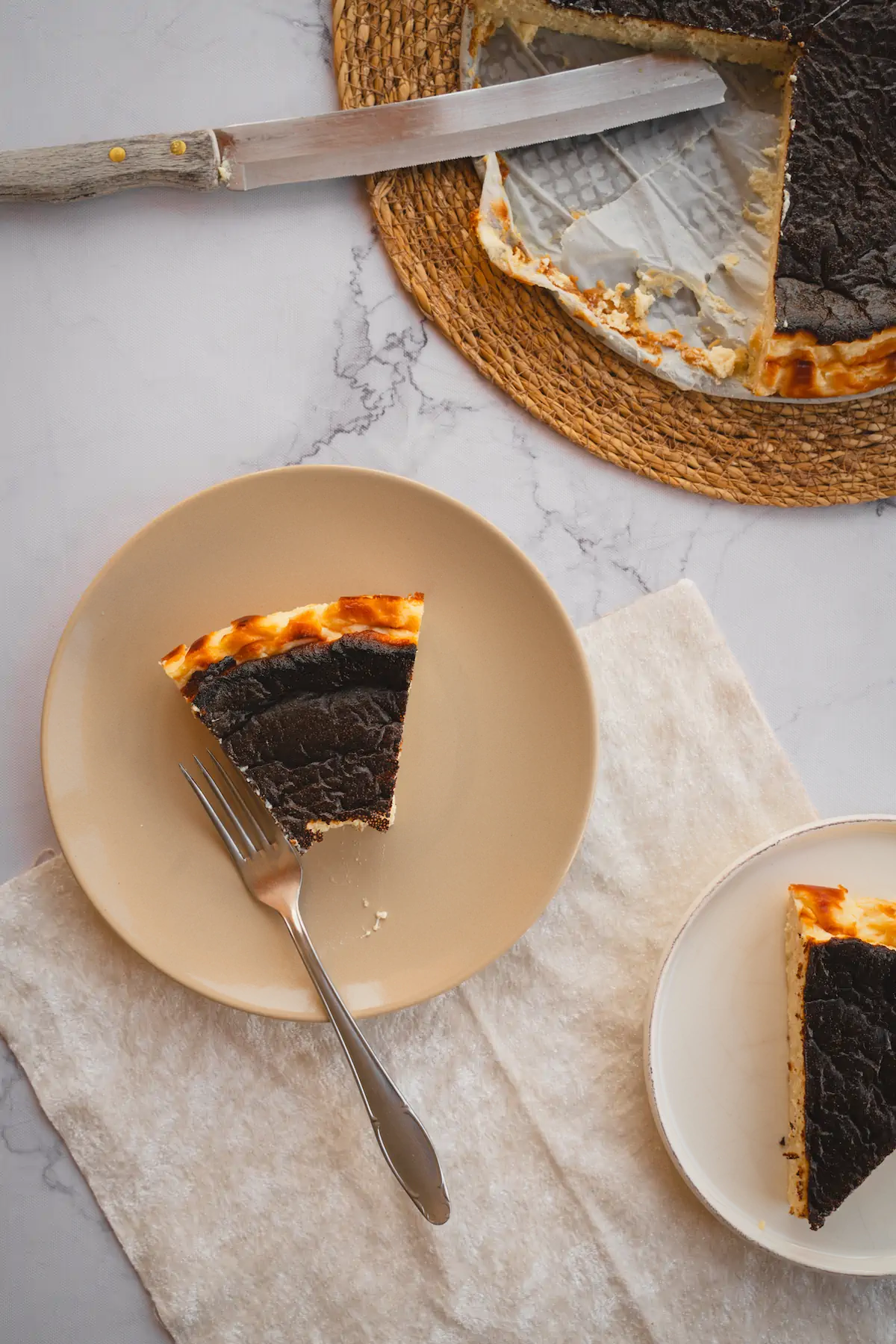 A slice of burnt Basque cheesecake on a plate, taken from the entire cake and a portion eaten with a fork.