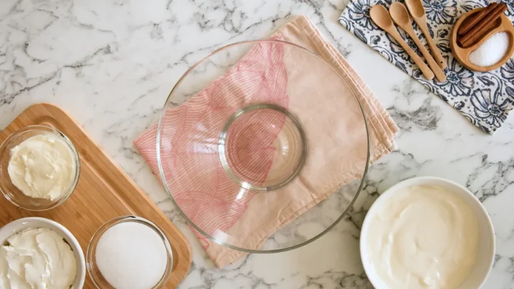 An empty bowl surrounded by cream cheese, monk fruit sweetener, eggs, heavy cream, and vanilla extract.