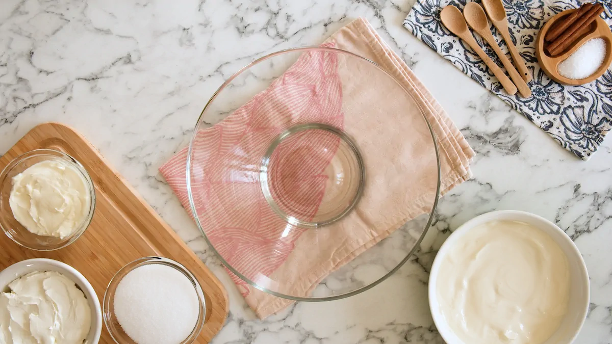 An empty bowl surrounded by cream cheese, monk fruit sweetener, eggs, heavy cream, and vanilla extract.