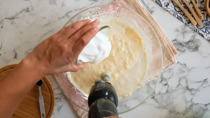 Adding heavy cream from a bowl to a cream cheese and monk fruit mixture.