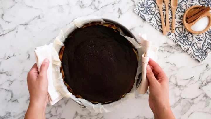 Freshly baked Basque cheesecake, held in a kitchen towel.