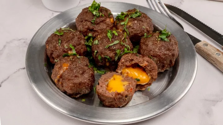 Meatballs filled with cheese served on a stainless steel plate, one cut open to show the melted cheese.