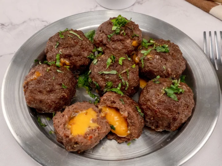 Homemade cheese-stuffed meatballs served on a stainless steel plate, with one cut open to display the melted cheese inside.