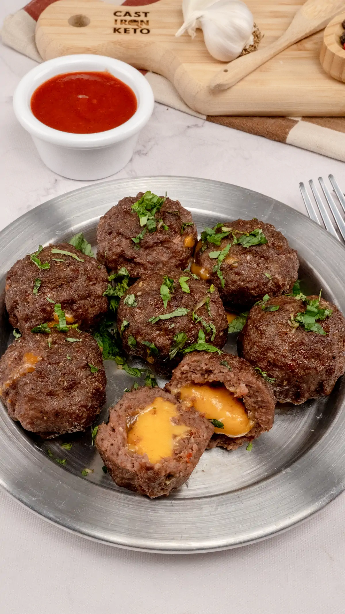 Cheese-filled meatballs served on a plate alongside a sauce in a bowl.