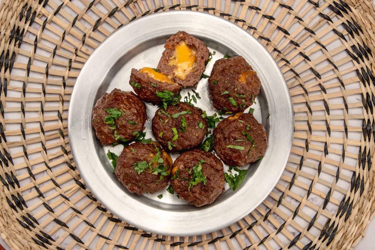 On a plate, cheese-filled meatballs are served, one cut open to display melted cheese.