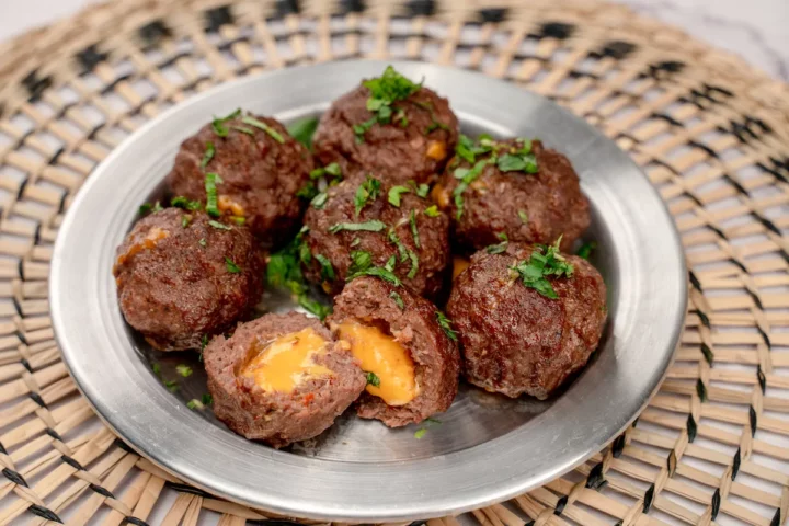 Cheese-stuffed meatballs on a plate, with one cut open to show the melted cheese.