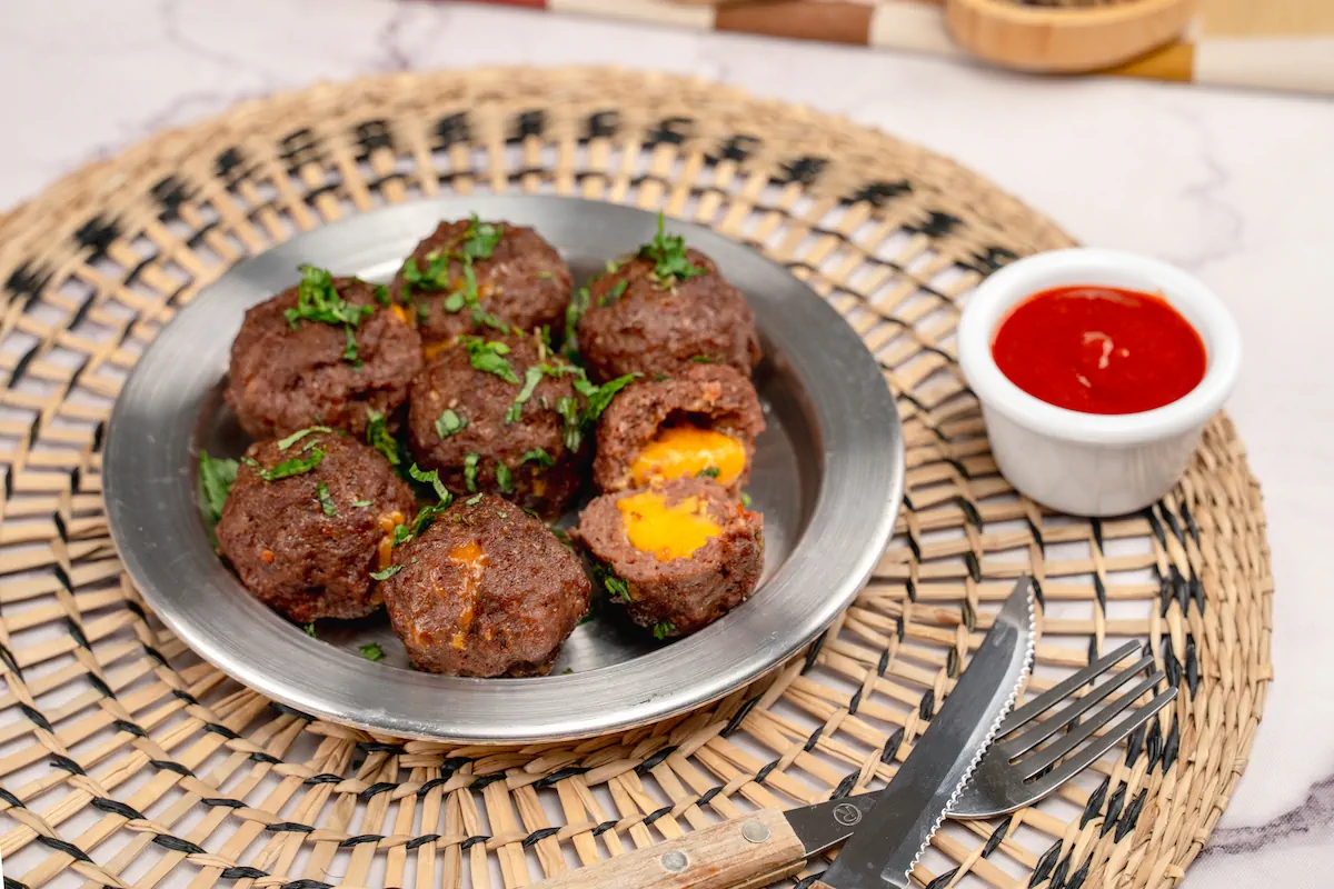Meatballs stuffed with cheese served with a small bowl of red sauce and cutlery.