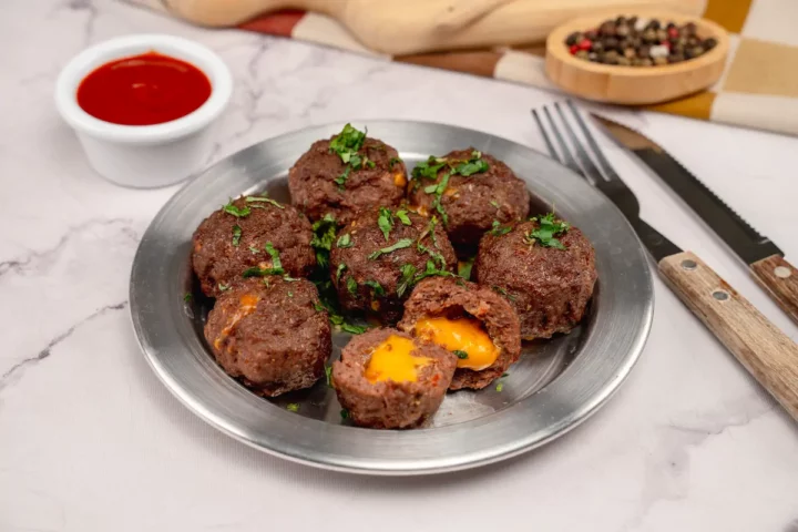 Cheese-stuffed meatballs served on a plate alongside a bowl of sauce and cutlery.