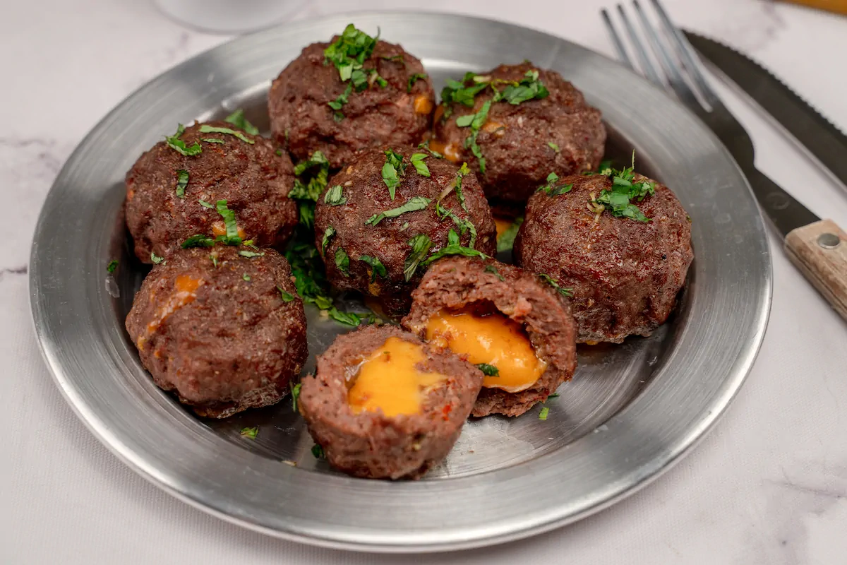 Closeup shot of cheese-filled meatballs served on a plate, with one cut open to showcase the melted cheese.