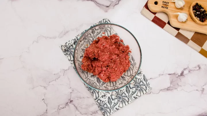 Ground beef mixed with spices in a transparent mixing bowl.