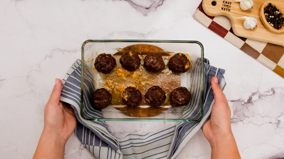 Placing cooked meatballs in a glass container on the kitchen counter with a towel.
