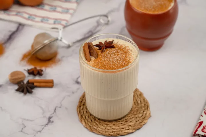 Keto eggnog presented in a transparent glass, adorned with cinnamon sticks and star anise, and dusted with cinnamon and nutmeg powder.