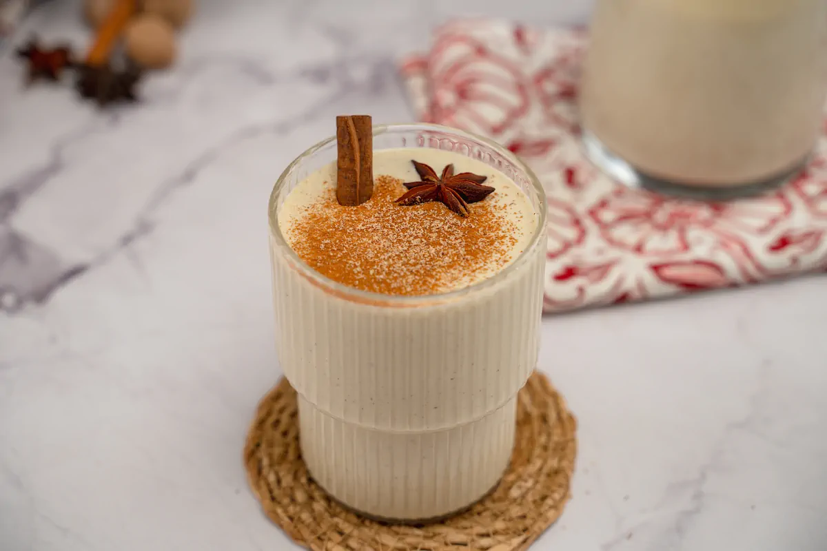 Homemade keto eggnog in a clear glass, adorned with cinnamon sticks, star anise, and a sprinkle of cinnamon and nutmeg powder.