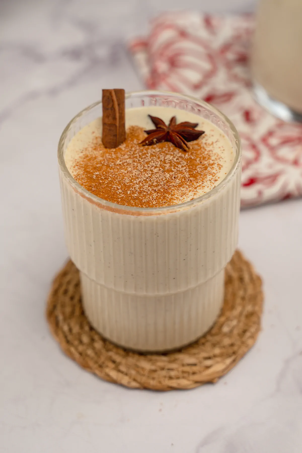 Low-carb eggnog served in a see-through glass with cinnamon sticks, star anise, and a sprinkle of cinnamon and nutmeg powder.
