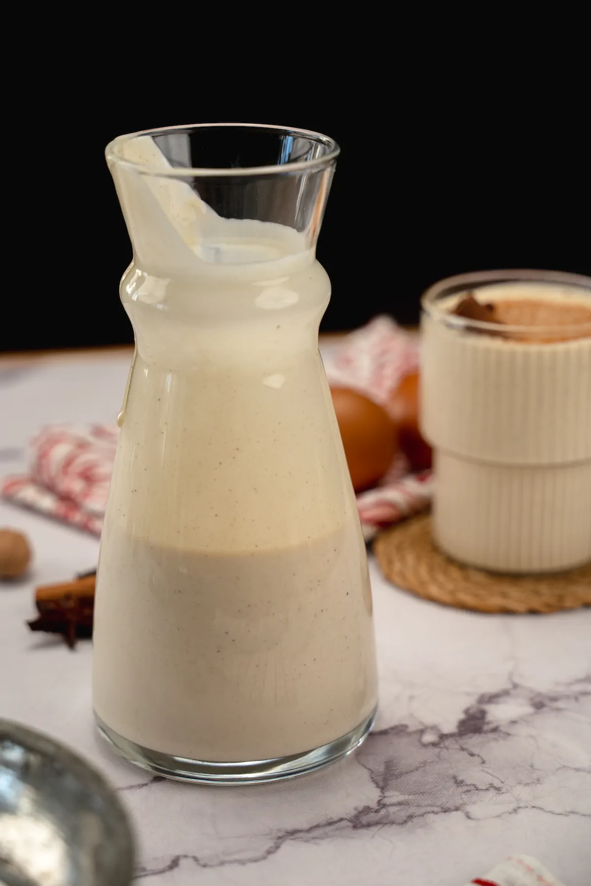 A glass jar half-filled with eggnog and a serving of eggnog is in the background.