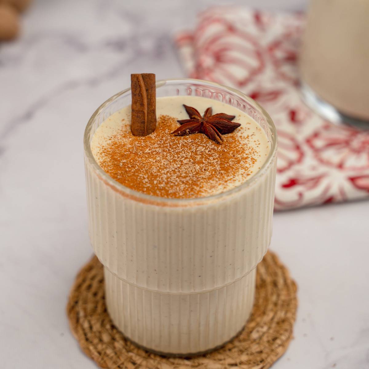 A transparent glass holding keto eggnog, garnished with cinnamon sticks, star anise, and cinnamon and nutmeg powder.