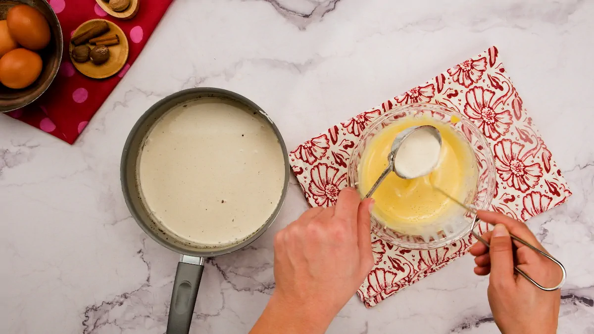 Pouring the heated cream mixture into a bowl with egg yolk and powdered erythritol mixture.