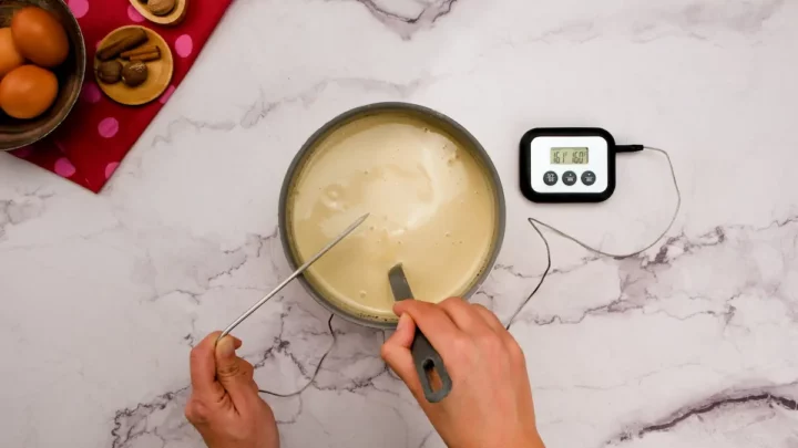 Checking the temperature of eggnog in a saucepan with a digital thermometer.